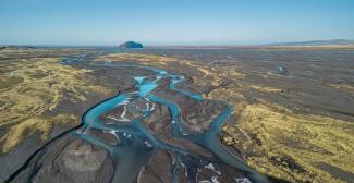 Aerial view of dry land with winding blue streams and a distant rock formation. Photo credit: Luca Ronchi via iStock.