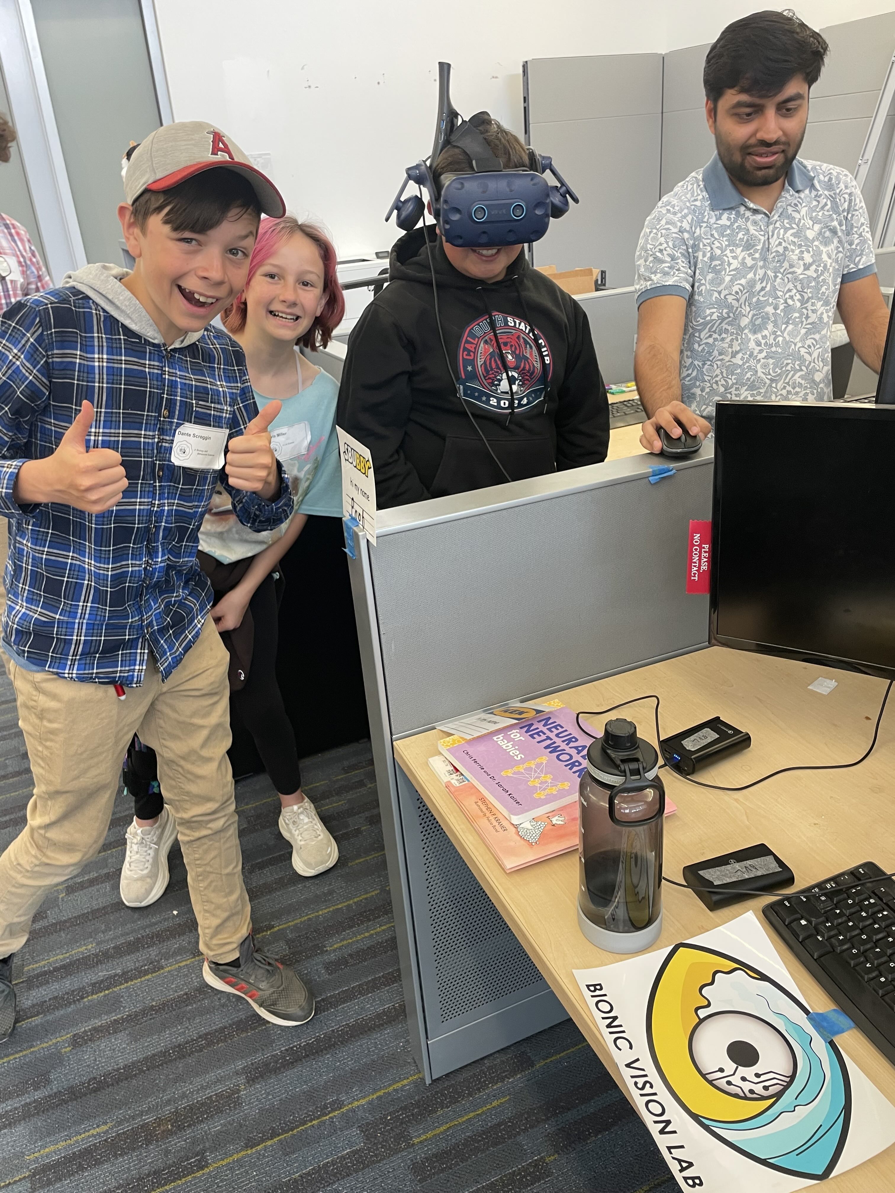 Students smile and give a thumbs-up while trying a virtual reality headset during a demonstration at the Bionic Vision Lab.