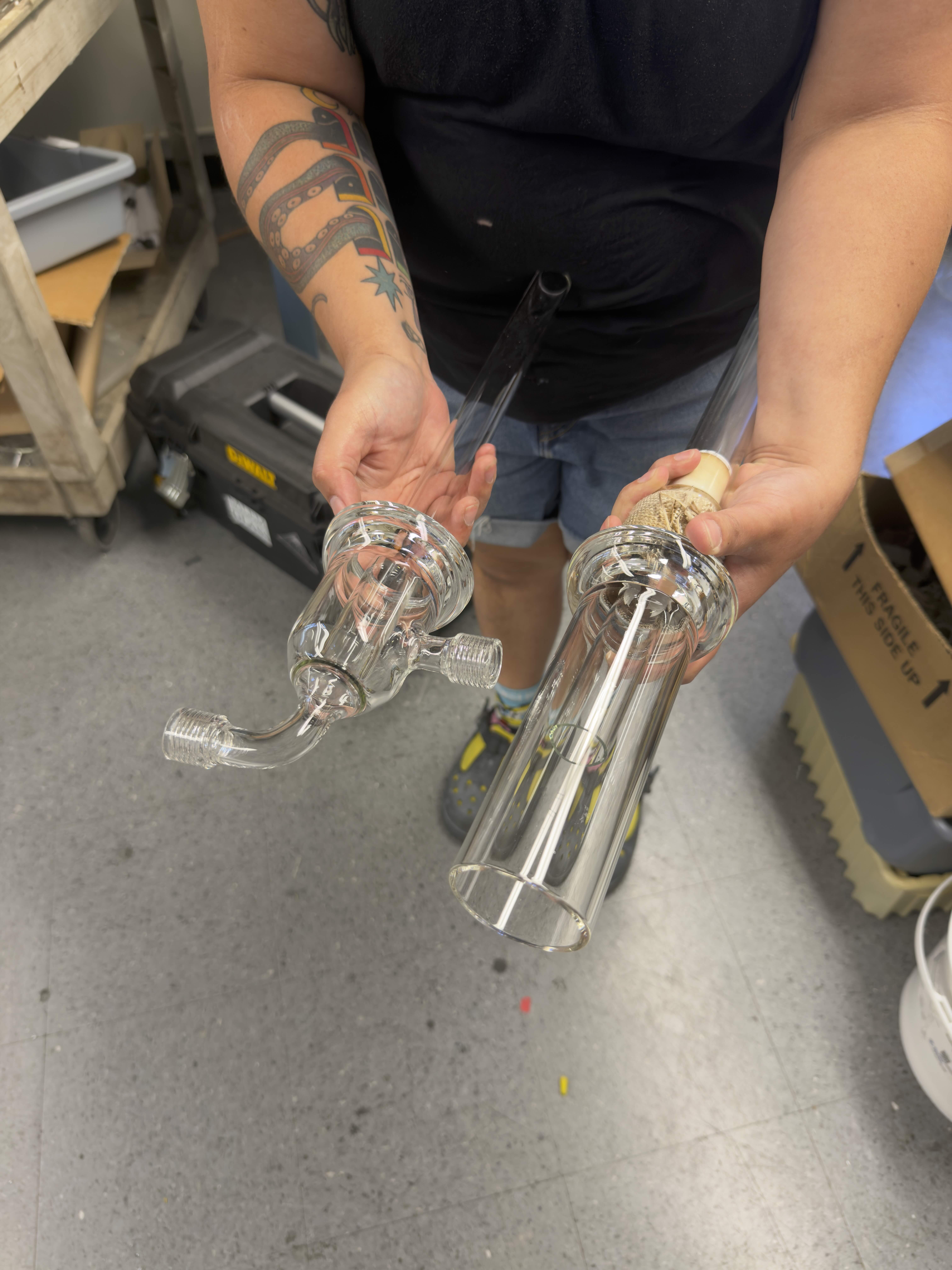 Corina Guerra holds two pieces of clear specialized scientific glassware in the UCSB Glass Shop.