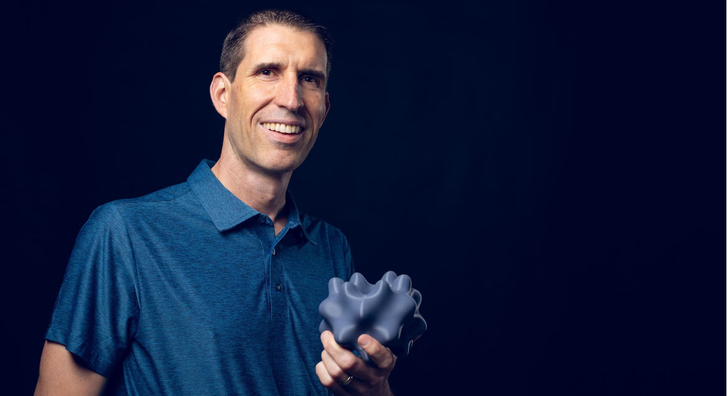 Paul Atzberger smiling and holding a gray, 3D-printed geometric object with multiple rounded protrusions.