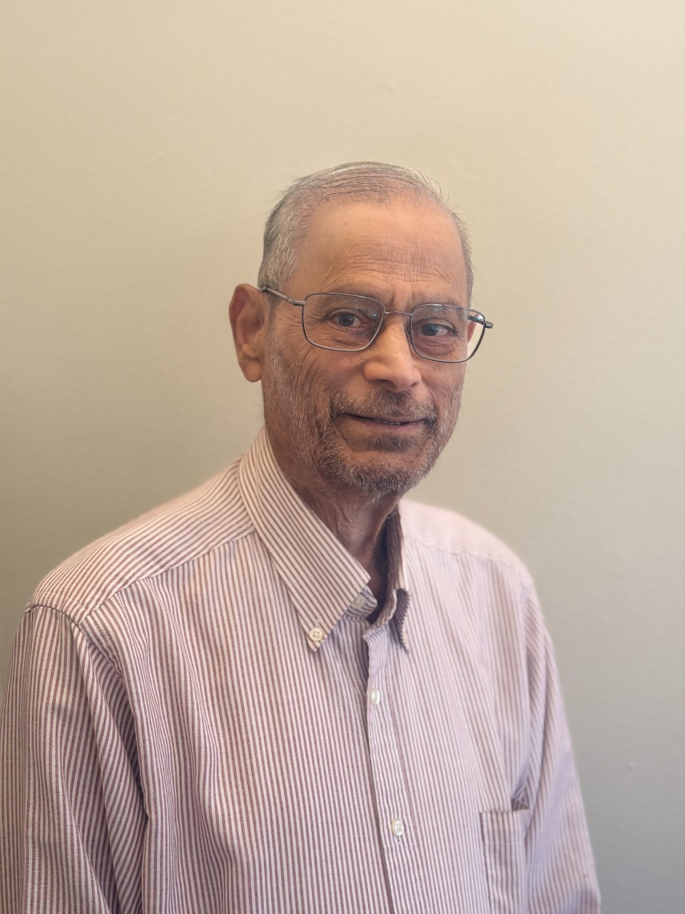 Distinguished Professor Sreenivasa Rao Jammalamadaka looking forward with a gentle smile, wearing a maroon and white striped shirt.