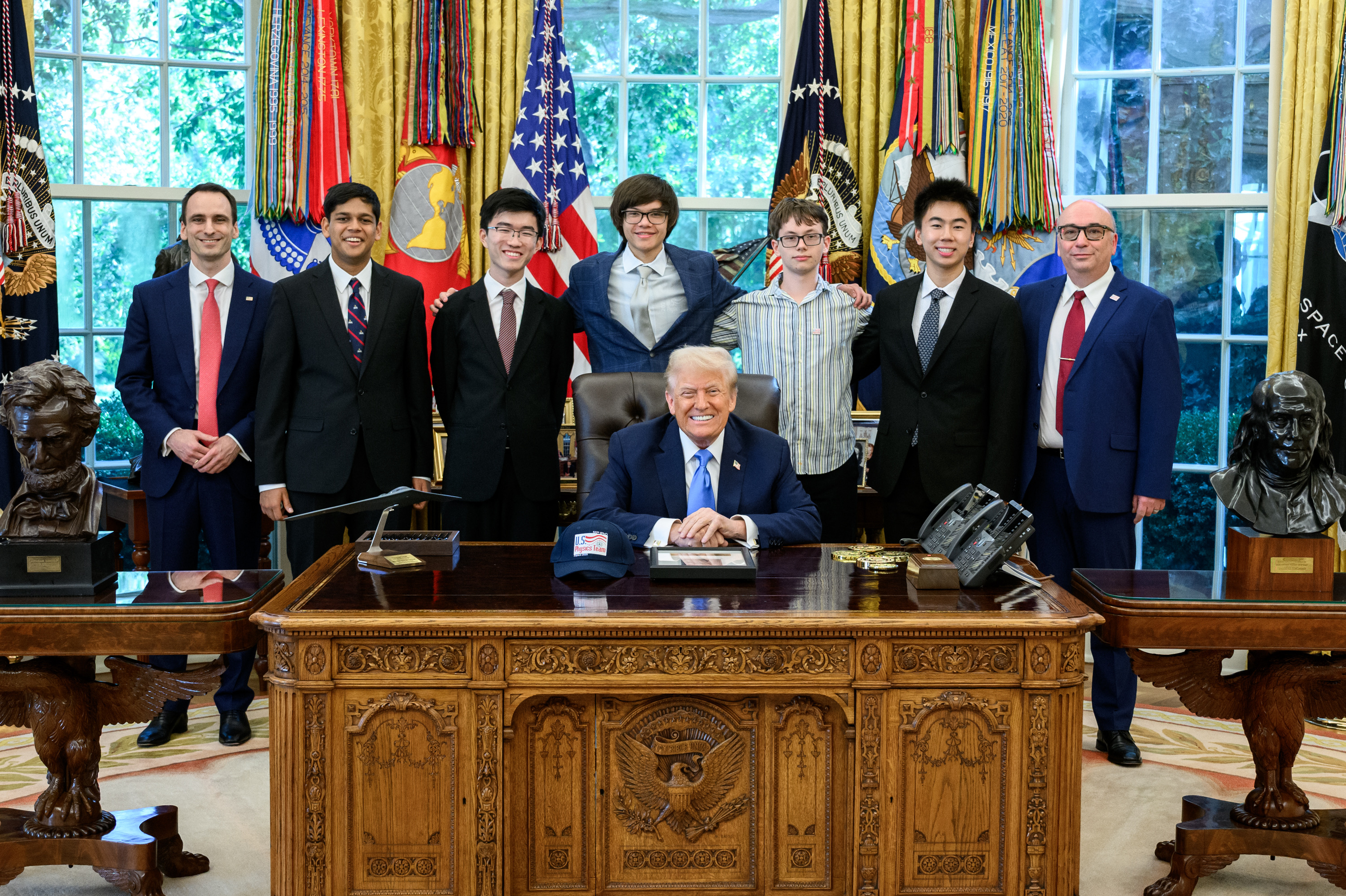 The President poses with the U.S. Physics Team and their coaches behind the Resolute Desk in the Oval Office.