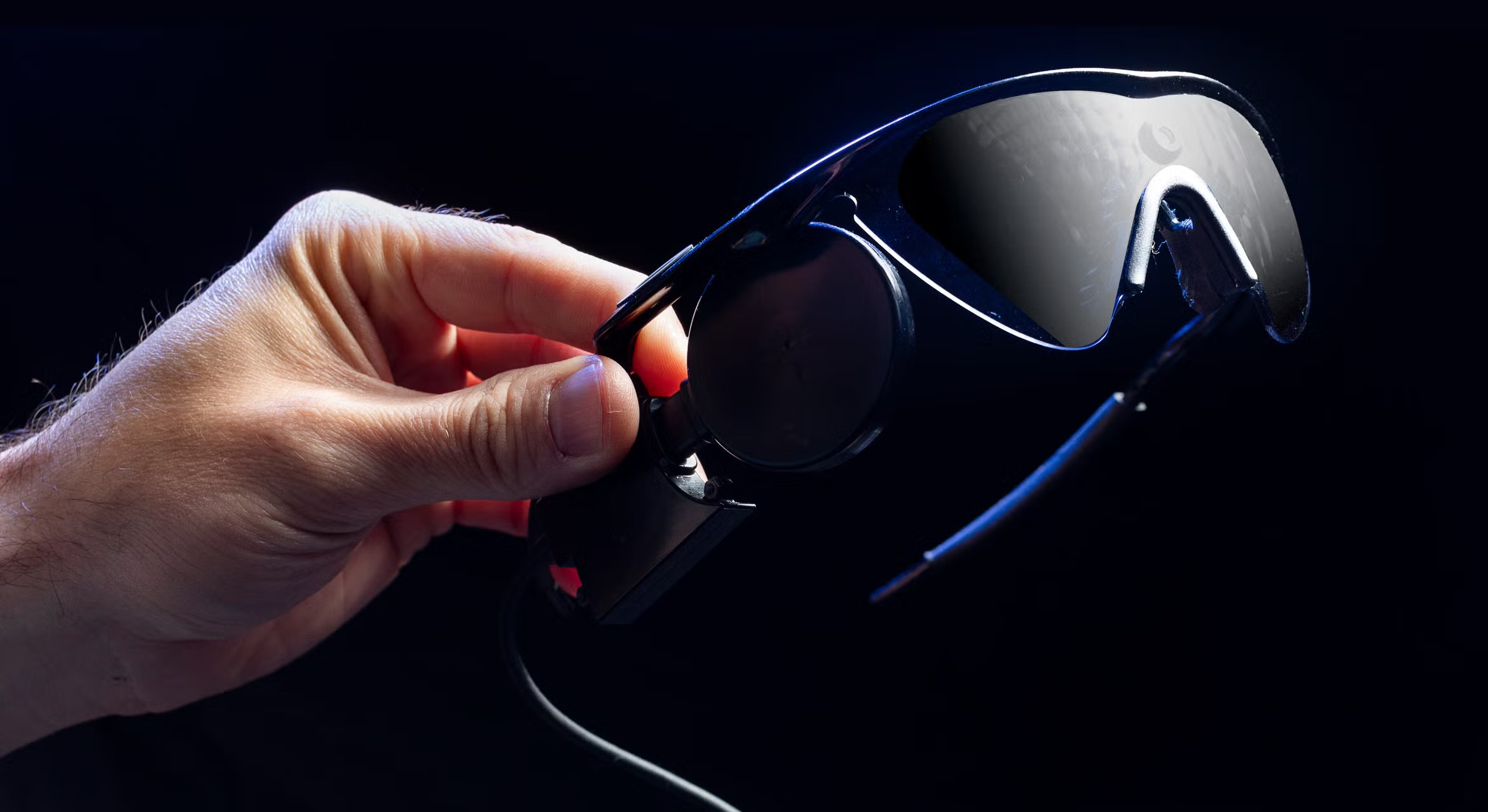 A hand holds a pair of prosthetic glasses used in bionic vision research.