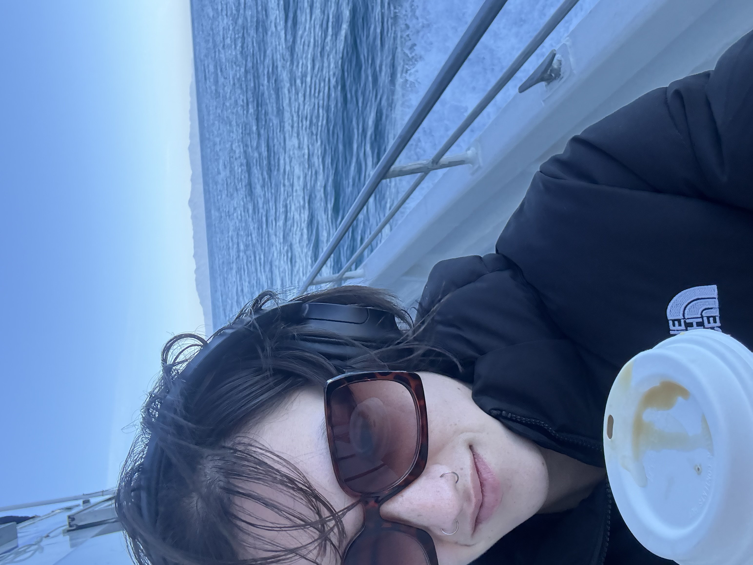 Undergraduate researcher Ava Jolly wearing sunglasses and headphones, smiling while riding a boat to the Channel Islands for field research.