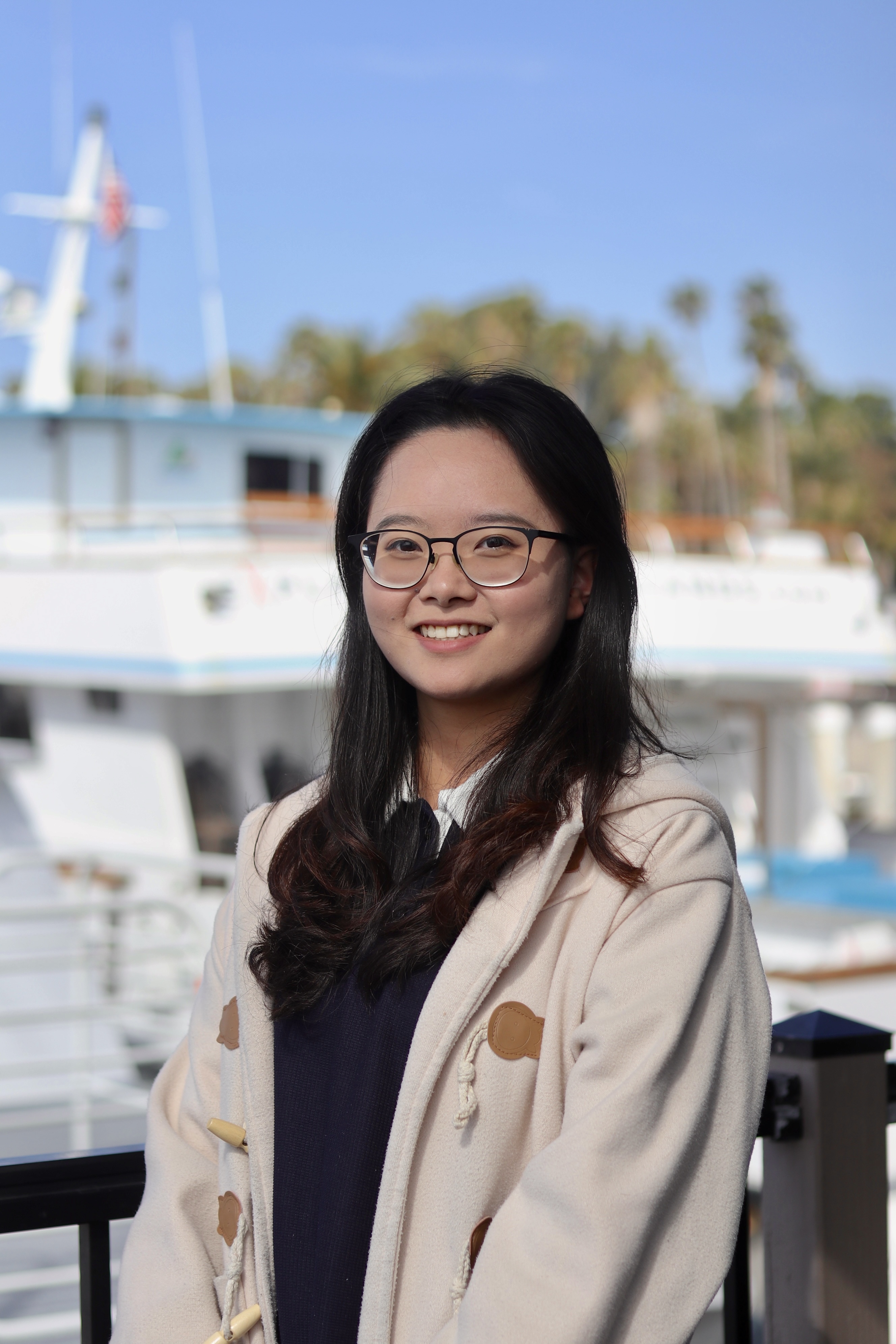 Qingyue (Jenny) Li smiling outdoors by a boat harbor.