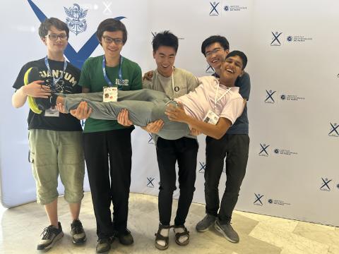 Four smiling students playfully lift a fifth team member in the air, showcasing their camaraderie.